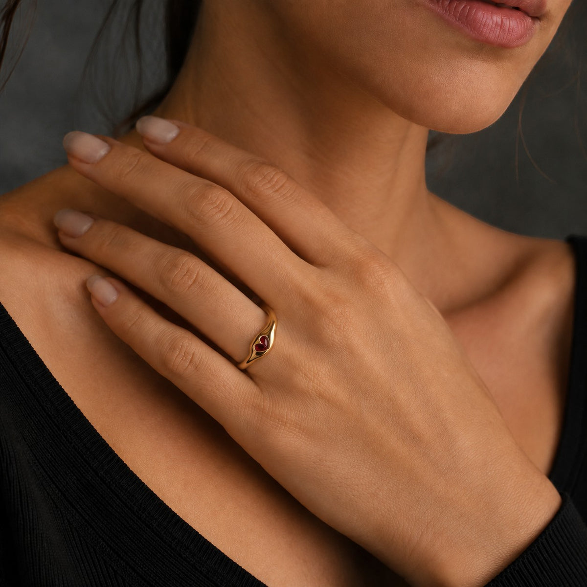 Meinara Bella ring featuring a gold sculpted band with a small red heart-shaped stone worn on a woman's finger