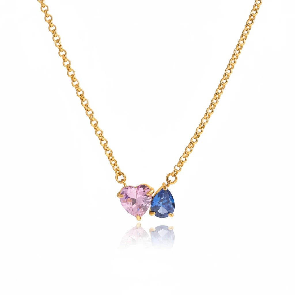 Meinara Maya necklace featuring a blush-pink heart-cut crystal and a deep-blue pear-cut crystal on a gold chain.